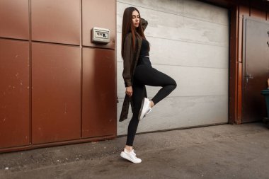 Genç güzel şık model kadın siyah tişört ve pantolon Beyaz Ayakkabı ve moda pelerin metal geçit yakın çekimde poz ile