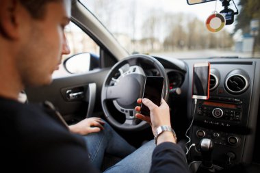 Adam bir arabanın direksiyonuna oturur ve bir akıllı telefon kullanır. Seyahat