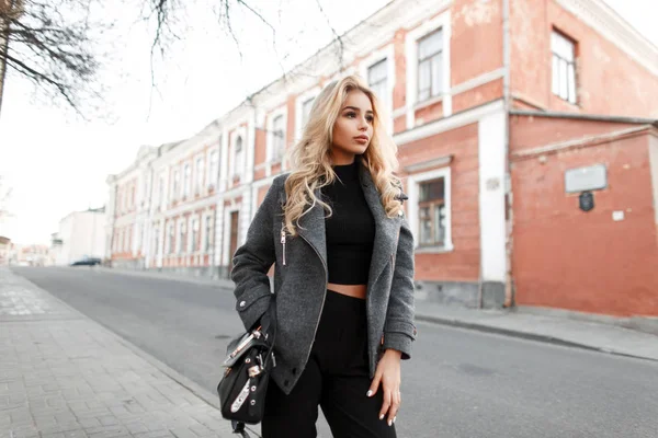 漂亮的年轻女子模特与时尚的黑色手提包在时尚夹克走在街上 — 图库照片