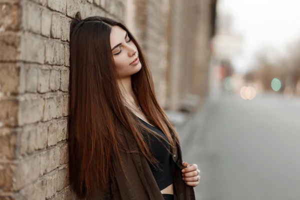 通りのレンガの壁の近くのトレンディな服の幸せな美しい若い女 — ストック写真