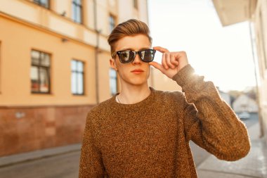 Yakışıklı moda genç adam kentin moda giysiler içinde günbatımında güneş gözlüğü takıyor