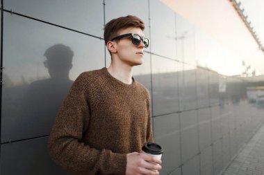 Kahve trendy şık kıyafetler moda yakışıklı modeli hipster adamla duvara yakın günbatımında duruyor.