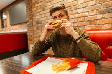 Genç adam hipster kapalı bir hamburger yemek