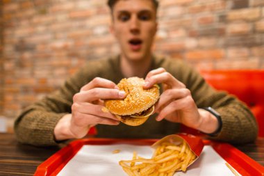 Adam bir duygu ile lezzetli bir hamburger yiyor. Yaşam tarzı lokanta.