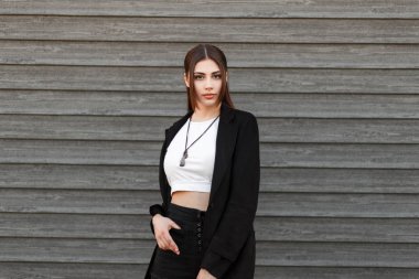 Genç ve güzel moda kadın siyah şık ceket ve beyaz bir T-shirt ayakta yakınındaki bir ahşap duvar sokak