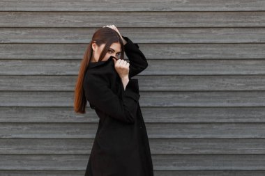 Yüzünü bir ahşap duvar arka planı siyah montlu genç moda modeli kız kapsar