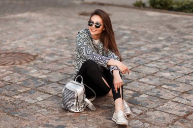Taş bir yol üzerinde oturan bir çanta moda giysiler bir gülümseme mutlu güzel kadın