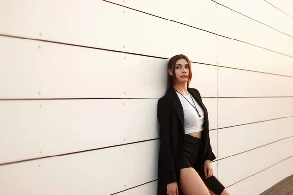 ショート パンツと黒のスタイリッシュなコートのファッション モデル女性が白い壁の近くに立って — ストック写真