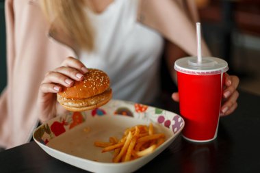 Genç kadın fast food yiyor: hamburger kola ve patates kızartması. Yakın çekim