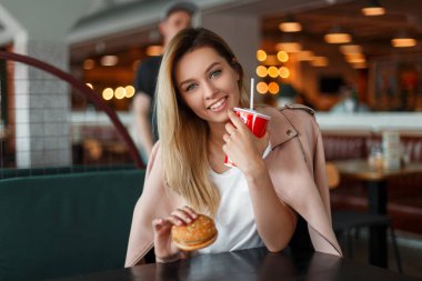 Komik güzel genç kadın bir lokanta hamburger yiyip kola içmeyi bir gülümseme ile