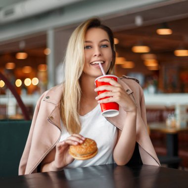 Bir hamburger ve bir bardak kola olan komik kadın bir kafede oturuyor
