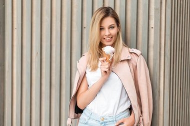 Bir gülümseme bir dondurma ahşap duvar yakınındaki bir yaz gününde yemek pembe moda ceket ile güzel mutlu kız