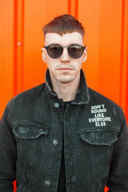 Yakışıklı genç Amerikalı adam bir turuncu duvarının yakınında siyah moda şık giysiler içinde bir saç modeli ile