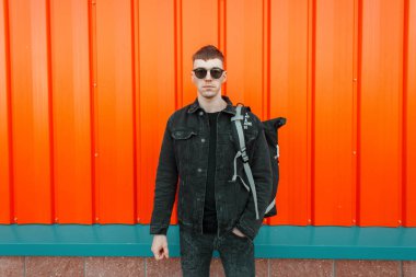 Yakışıklı şık genç bir siyah kot ceket bir sırt çantası ile gözlüklü adam sokakta model.