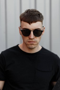 güneş gözlüğü ve siyah T-shirt gri metal duvarın yanında kötü bir ruh ile şık genç adam