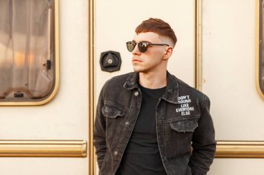 Yakışıklı genç adam sahilde vintage bir römork yakınındaki siyah moda giysileri ile şık güneş gözlüğü