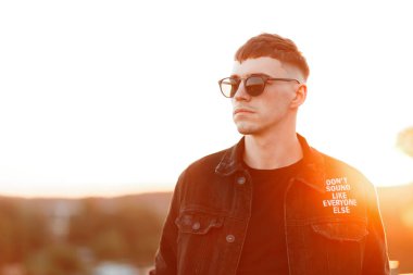Moda yakışıklı genç Amerikalı manken adam siyah şık denim elbiseleri günbatımı
