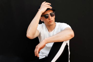 Bununla birlikte güneş gözlüklü bir beyaz moda ile siyah şapkalı şık yakışıklı delikanlı t-shirt siyah bir arka plan üzerine oturur.
