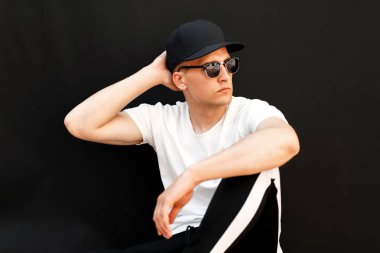 Beyaz bir T-shirt ve modaya uygun pantolon siyah bir arka plan üzerine siyah şapkalı gözlüklü bir adam şık genç modeli