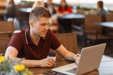 Kahve içme ve kafede dizüstü bilgisayar üzerinde çalışan genç yakışıklı adam blogger