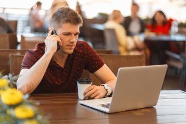 Genç blogger adam ile bir dizüstü bilgisayar ve kentin bir kafede bir smartphone cep telefonu ile arama yapma kahve