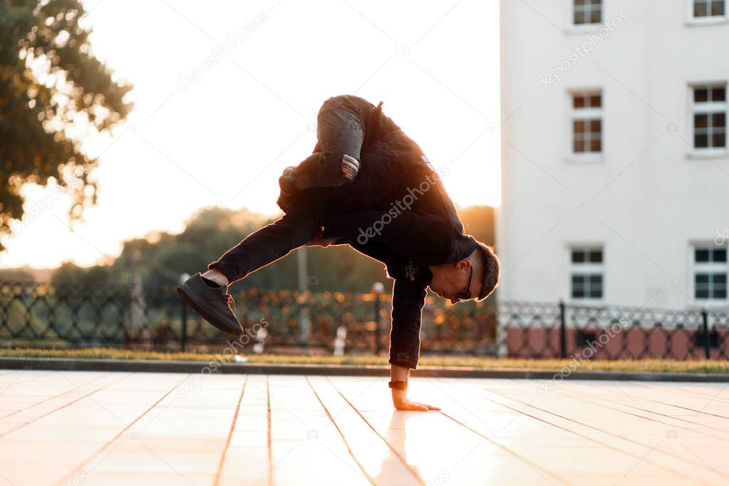 Young stylish male dancer in black denim clothes dancing at sunset