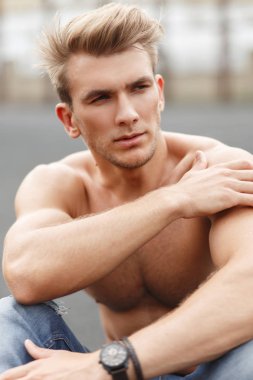 Yakışıklı Amerikalı genç manken adam sokakta asfalt üzerinde oturan kasları ile sağlıklı fitness vücut ile şık bir saç modeli ile