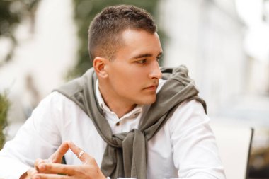 Şehirde bir kafede bir kazak ile beyaz bir gömlek moda yakışıklı genç adam oturur