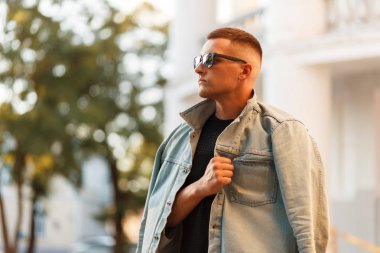 Şık yakışıklı delikanlı bir kot ceket ve siyah T-shirt şehirde poz güneş gözlüklü bir saç modeli ile