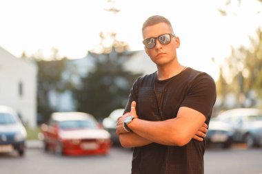 Şık yakışıklı genç moda güneş gözlüğü gün batımında sokakta siyah T-shirt bir saç modeli ile