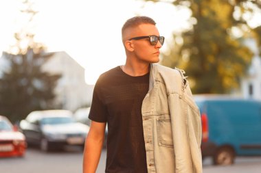 Şık güzel model hipster adam siyah moda T-shirt ve şehirde yürüyüş bir vintage kot ceket güneş gözlüklü bir saç modeli ile