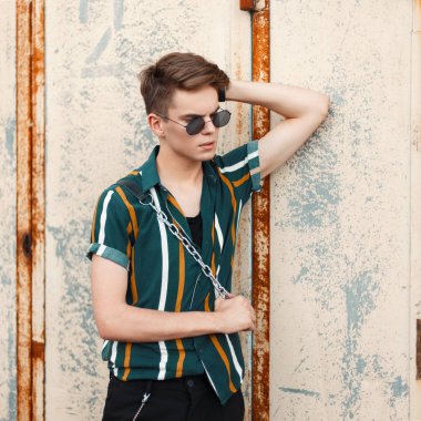 Genç yakışıklı modeli adam trendy güneş gözlüklü bir saç modeli ve gözde plaj gömlek ile bir metal duvar standları