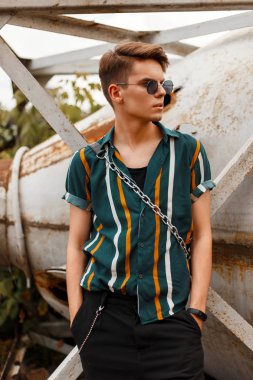 Plaja yakın bir metal vintage kap bir çanta ile şort ile şık bir gömlek içinde güneş gözlüğü ile şık yakışıklı genç erkek modeli