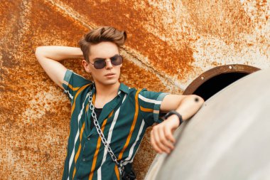 Moda model erkek güneş gözlüğü renk plaj moda gömlekli bir paslı duvarının yakınında şık bir saç modeli ile
