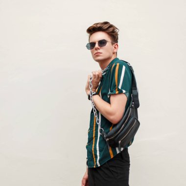 Duvarın yanında bir çanta çizgili gömlekli siyah gözlüklü moda yakışıklı genç adam