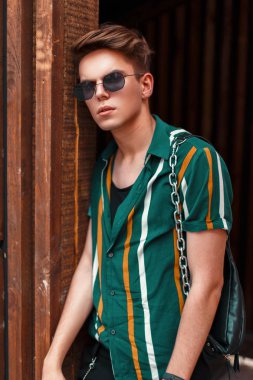 Güzel genç şık adam ahşap duvar yakınındaki popüler plaj giysili bir saç modeli ile