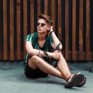 Yaz moda giysileri ahşap bir duvara yakın oturan bir saç modeli ile yakışıklı genç