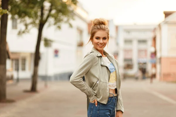 Beautiful young happy woman with a natural smile in a fashionable jacket with jeans walking in the city.