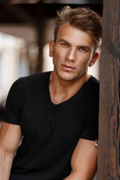 屋外木製柱の近く黒のスタイリッシュな シャツで髪型とハンサムな若い男性モデル — ストック写真