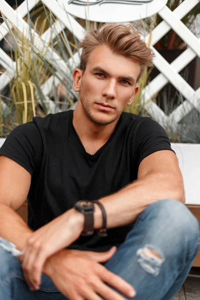 saçlı siyah T-shirt ve kot sahilde oturan bir moda şık genç adam