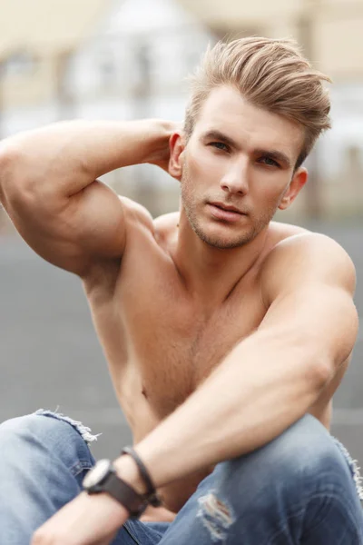 Yakışıklı şık fitness model adam sokakta oturan sağlıklı bir vücut ile bir saç modeli ile
