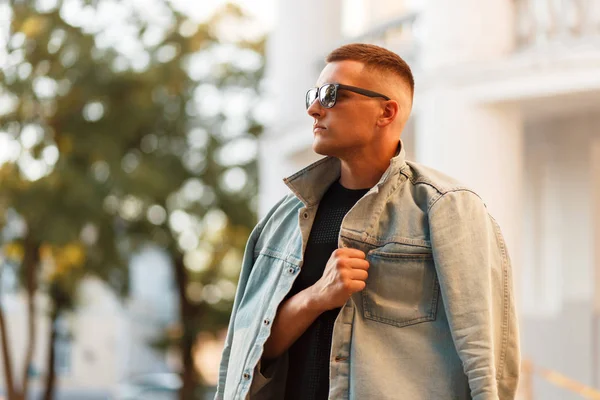 Şık yakışıklı delikanlı bir kot ceket ve siyah T-shirt şehirde poz güneş gözlüklü bir saç modeli ile