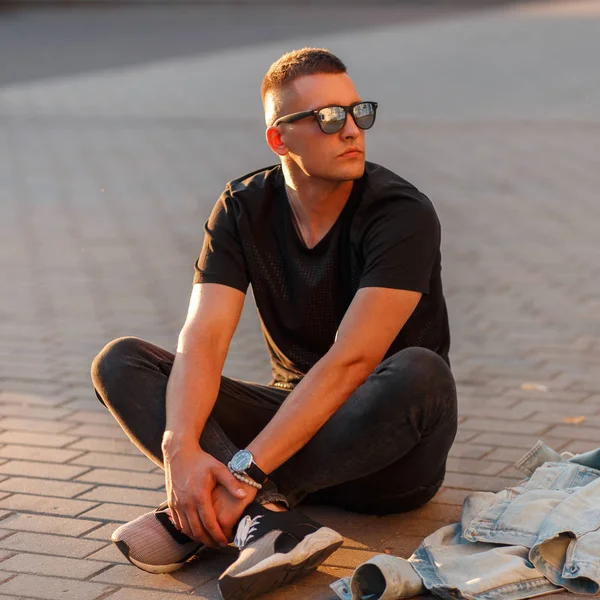 Moda yakışıklı genç modeli içinde sokakta oturan siyah şık T-shirt Siyah güneş gözlüğü