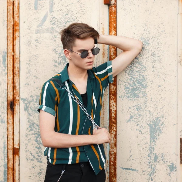 Genç yakışıklı modeli adam trendy güneş gözlüklü bir saç modeli ve gözde plaj gömlek ile bir metal duvar standları