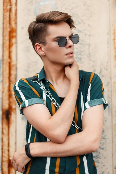 Güneş gözlüğü ve gözde plaj gömlek metal duvar yakınındaki bir çanta içinde bir saç kesimi ile şık genç adam