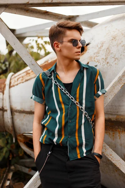 Plaja yakın bir metal vintage kap bir çanta ile şort ile şık bir gömlek içinde güneş gözlüğü ile şık yakışıklı genç erkek modeli