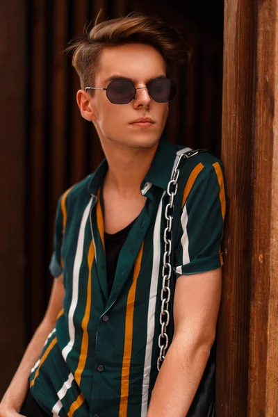 Ahşap duvar yakınındaki bir vintage beach gömlekli gözlüklü şık genç yakışıklı adam
