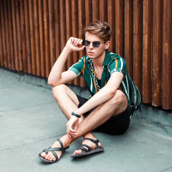 Şık yakışıklı genç moda yaz giysileri sokakta oturan bir saç modeli ile