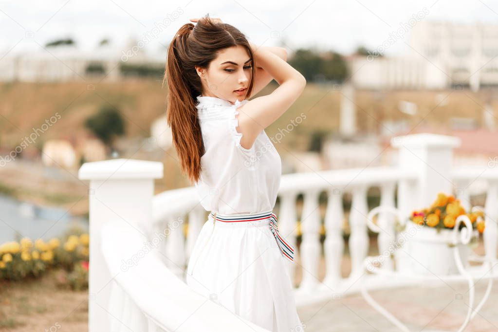 Fashionable young model woman in white dress posing near white fencing