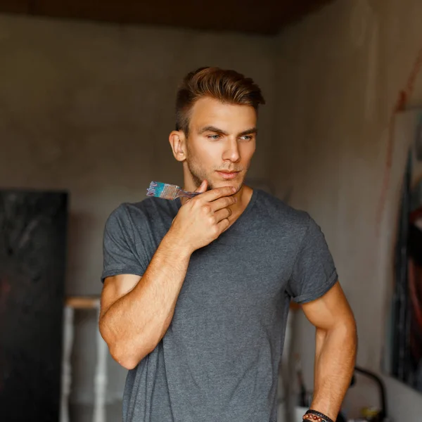 Young talented man with a brush in a gray T-shirt in an art stud — Stock Photo, Image